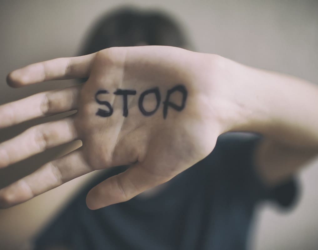 A person holds out their hand with the word "STOP" written on the palm in black ink.