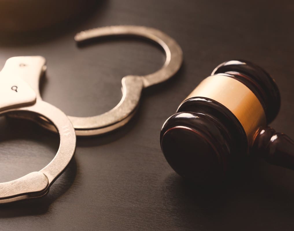 A pair of handcuffs lies next to a wooden judge's gavel on a dark surface.