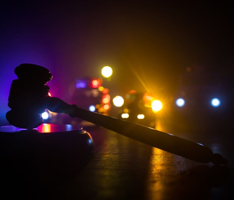 A gavel rests on a surface with blurred police car lights in the background.