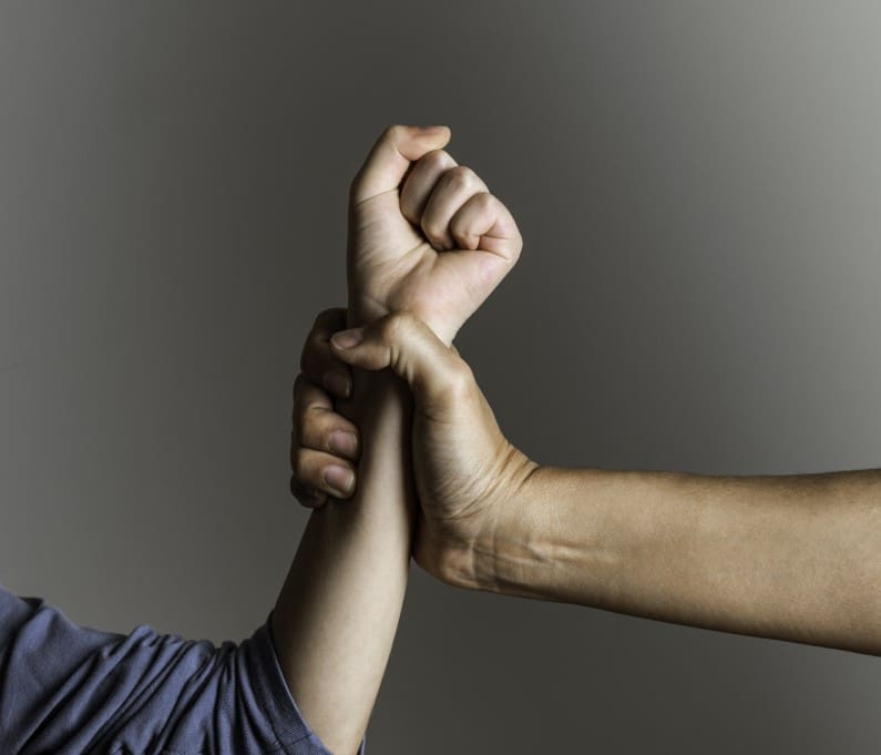 A hand grips another person's wrist firmly against a neutral background.