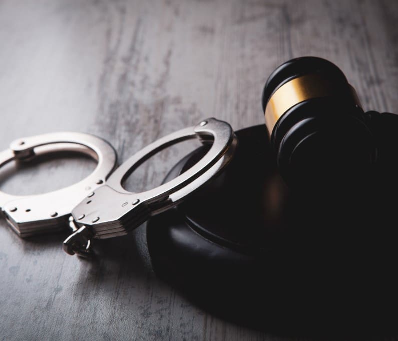 Handcuffs and a judge's gavel on a wooden surface, symbolizing law and justice.