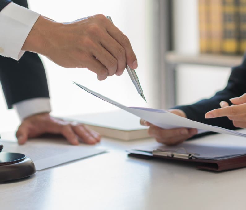 Two people in formal attire are discussing and pointing at documents on a table.