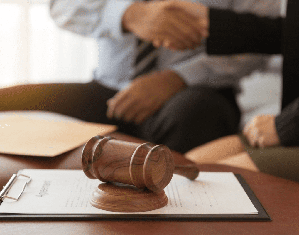 A gavel rests on a document labeled "Agreement," with two people shaking hands in the blurred background.